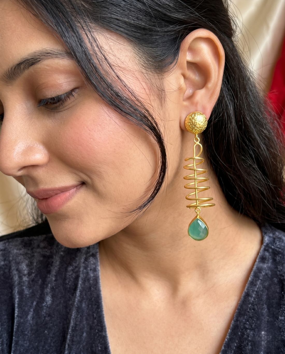 Close-up of a woman wearing gold spiral earrings with a green teardrop pendant.