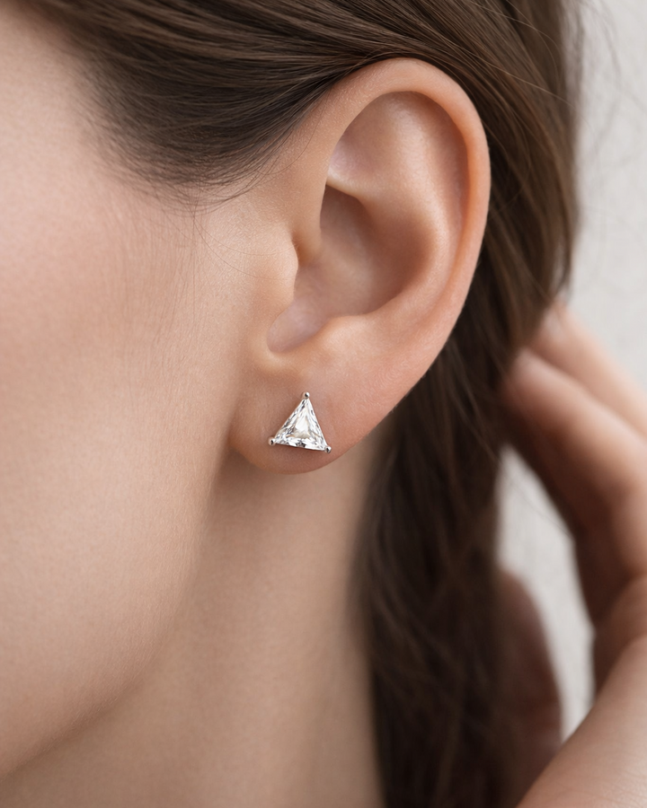 Close-up of an ear wearing a triangle-shaped stud earring with blurred background