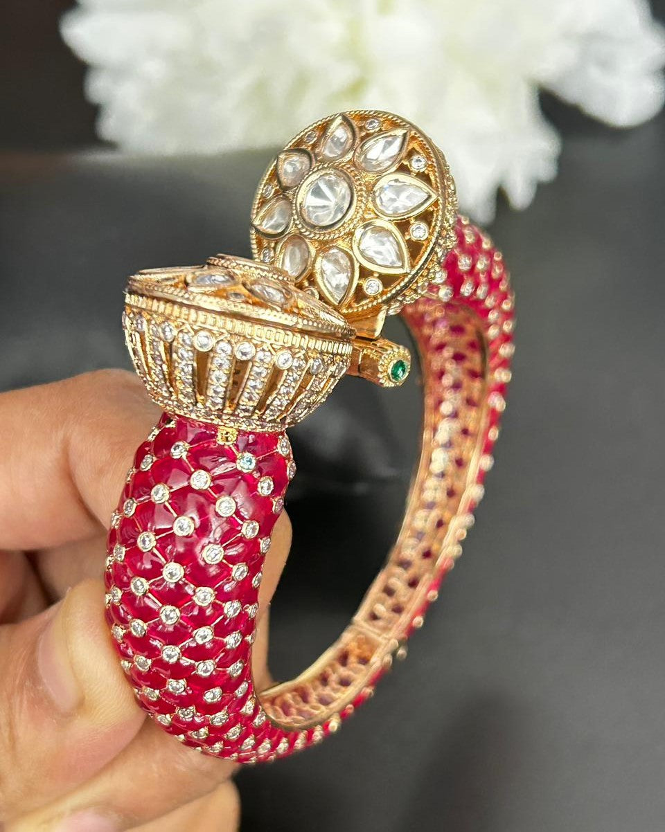 Decorative bangle with intricate design held by a hand against a blurred floral background
