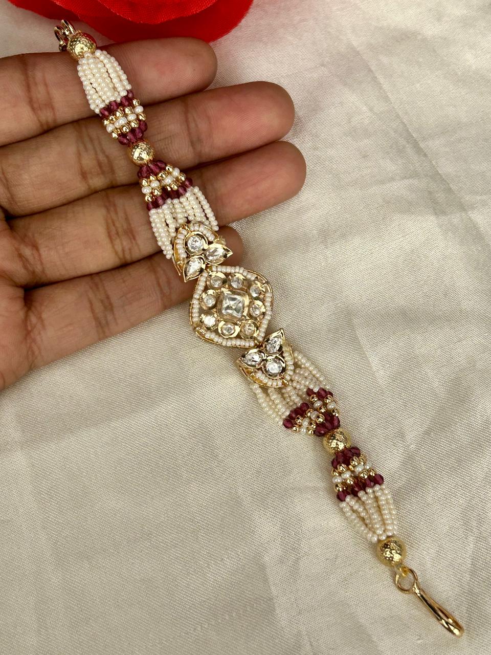 Decorative beaded bracelet with gold and red accents on a hand against a light fabric background