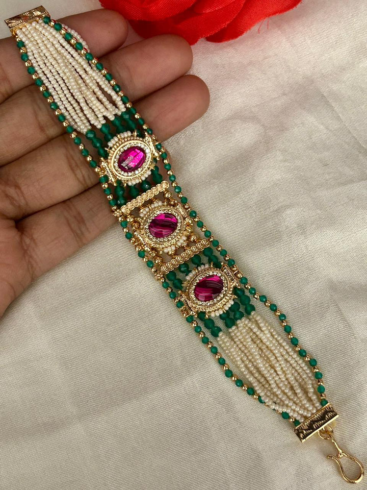 Decorative bracelet with green and gold beads and pink gemstones on a hand.