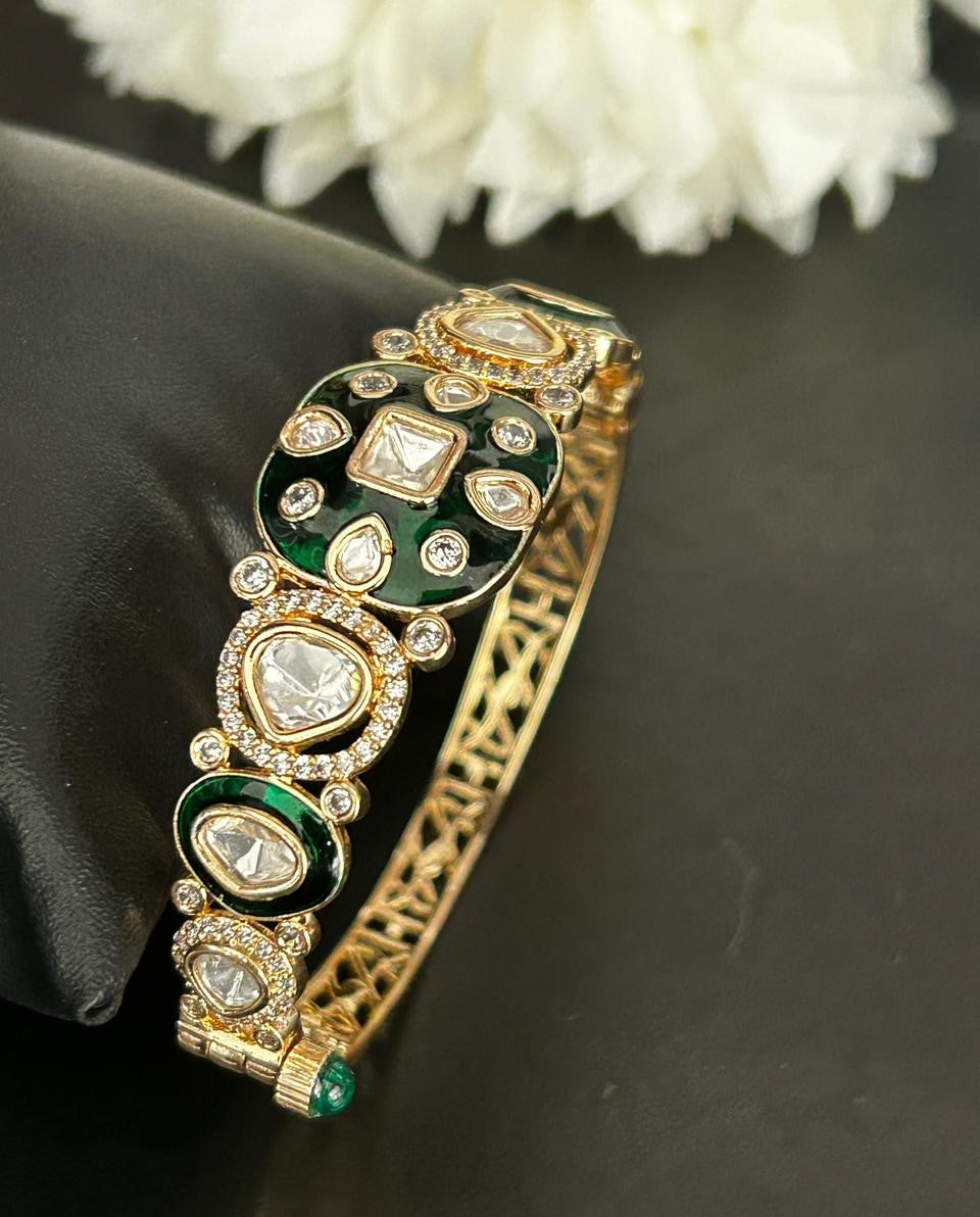 Decorative bracelet with green and gold design on a dark surface with white flowers in the background