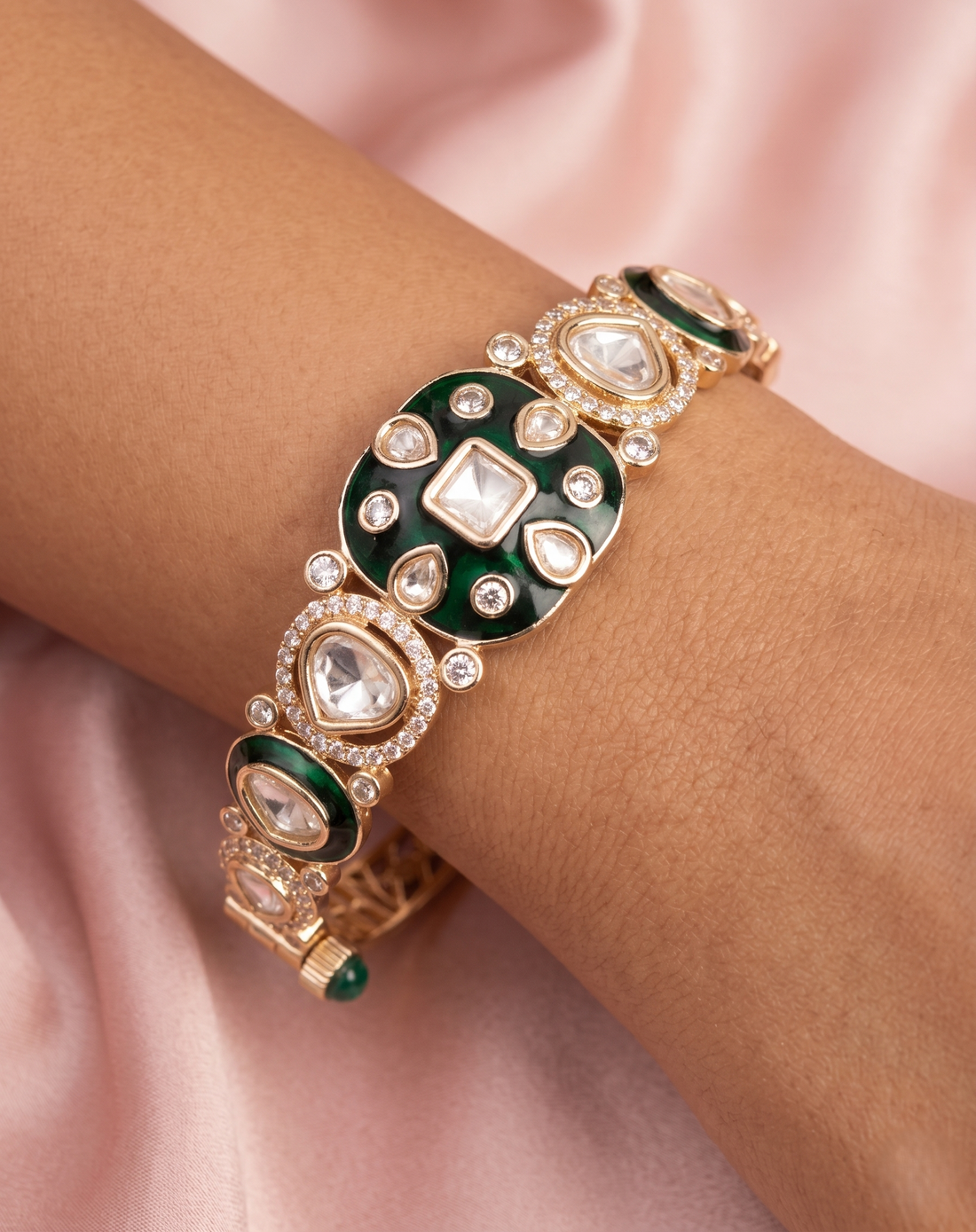 Decorative bracelet with green and gold elements on a wrist against a soft pink background