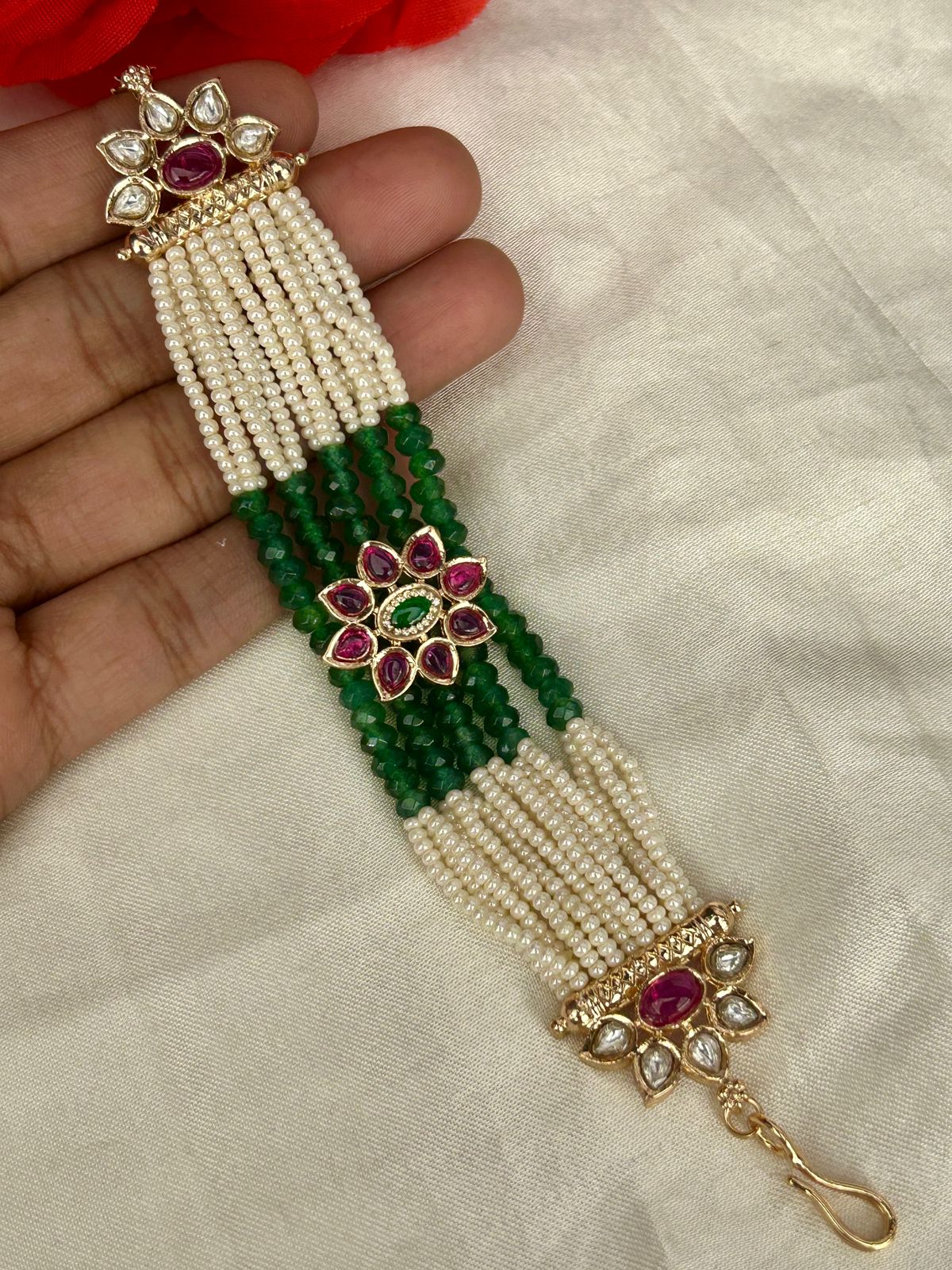Decorative bracelet with green and white beads and red gemstones on a neutral background