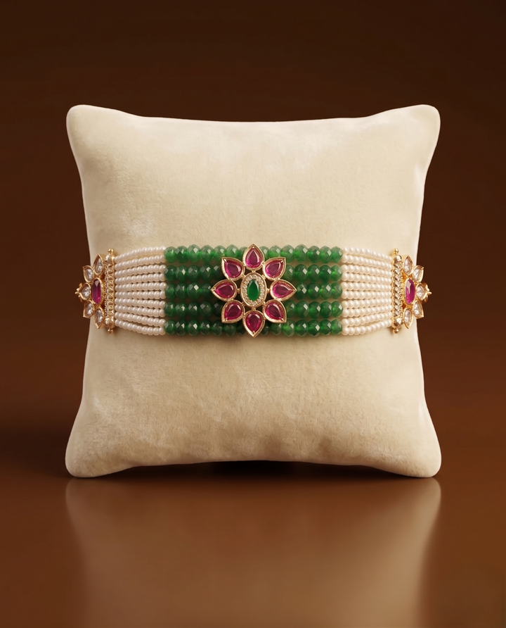 Decorative bracelet with green beads and floral design on a beige pillow against a brown background