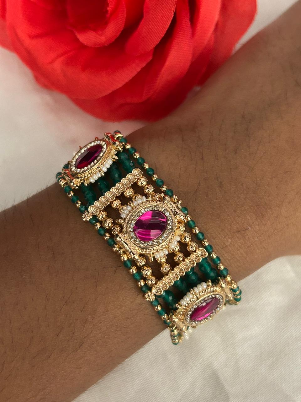 Decorative bracelet with pink and green stones on a wrist, against a red flower background.