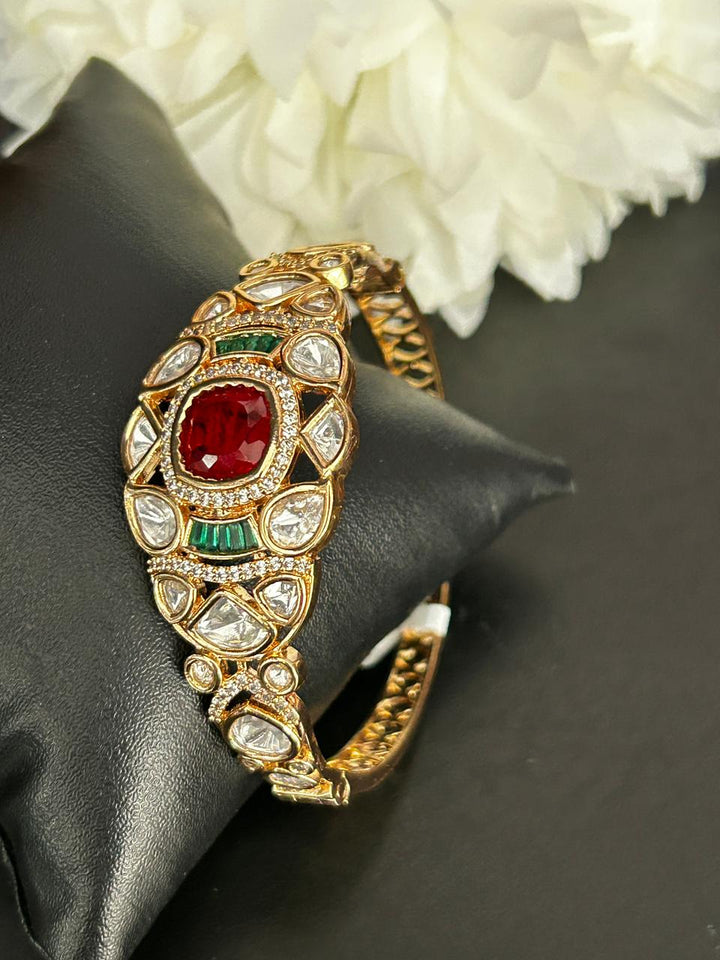 Decorative bracelet with red and green gemstones on a black surface with white flowers in the background