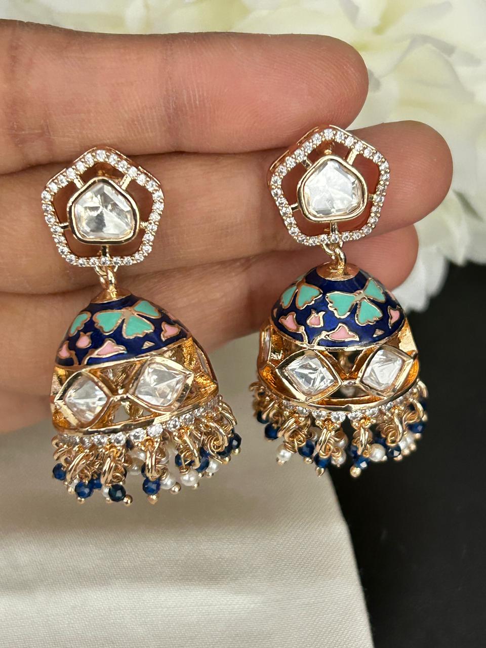 Decorative earrings held between fingers with a blurred floral background