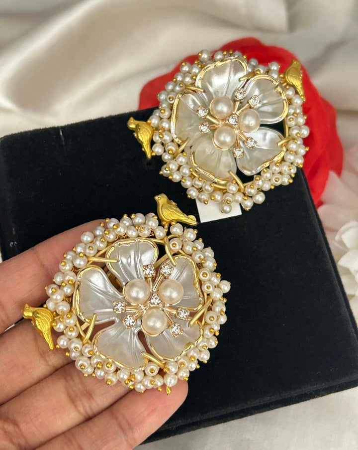 Decorative earrings with floral design and pearl embellishments on a black box.