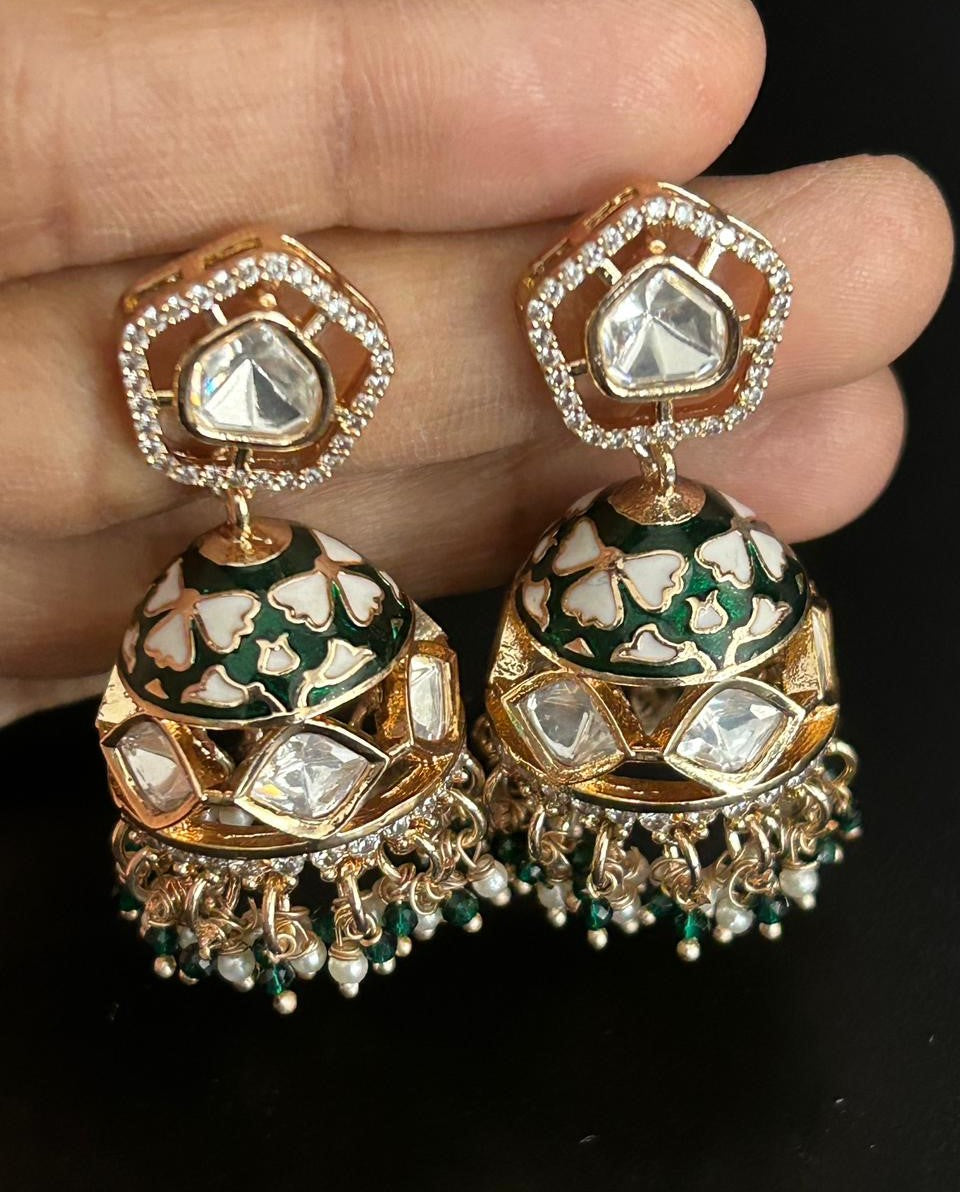 Decorative earrings with green and gold details held by a hand against a black background