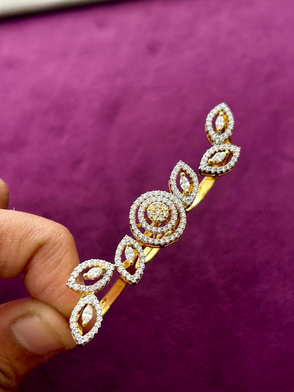 Decorative gold and diamond bracelet held by a hand against a purple background