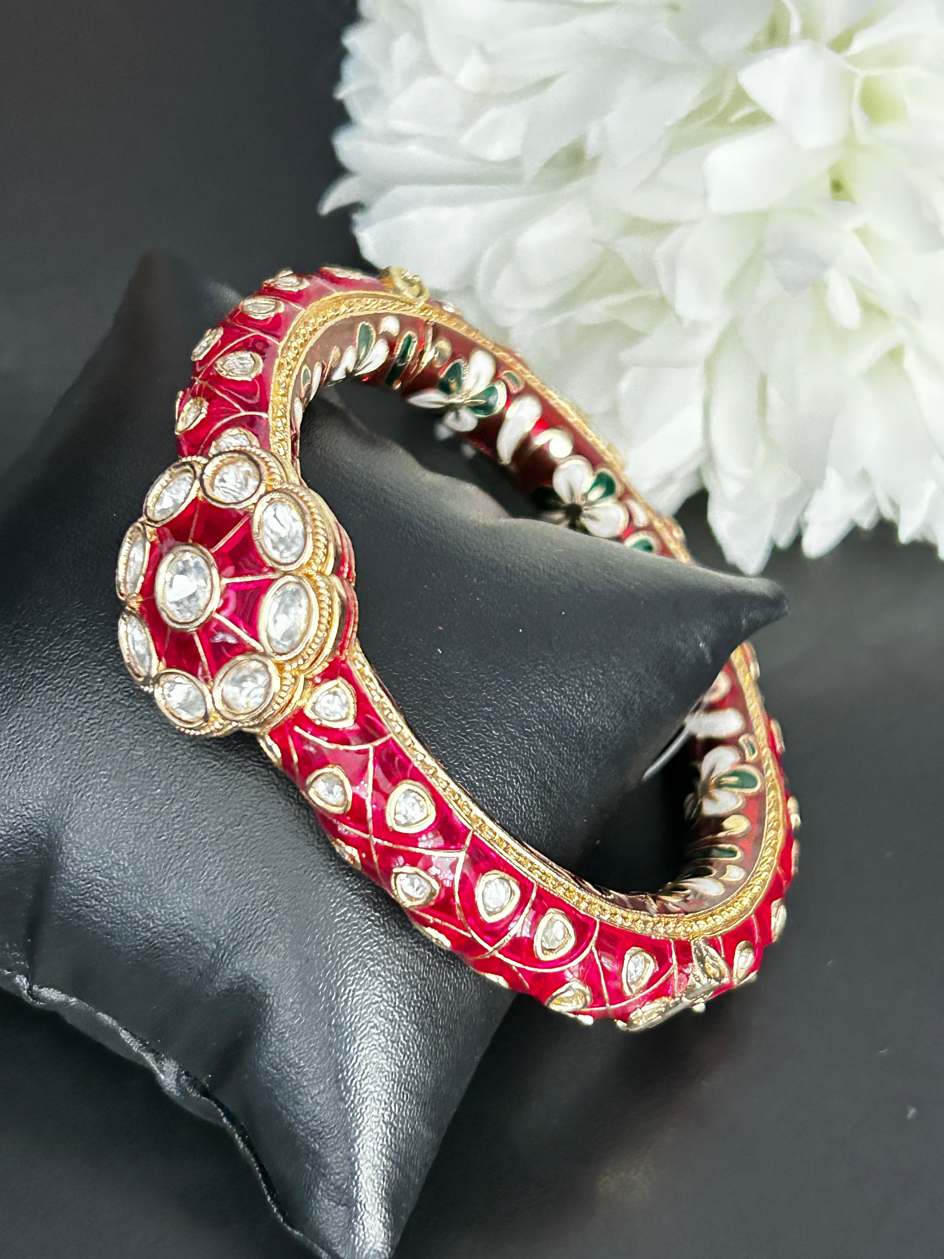 Decorative red and gold bangle on a black surface with white flowers in the background
