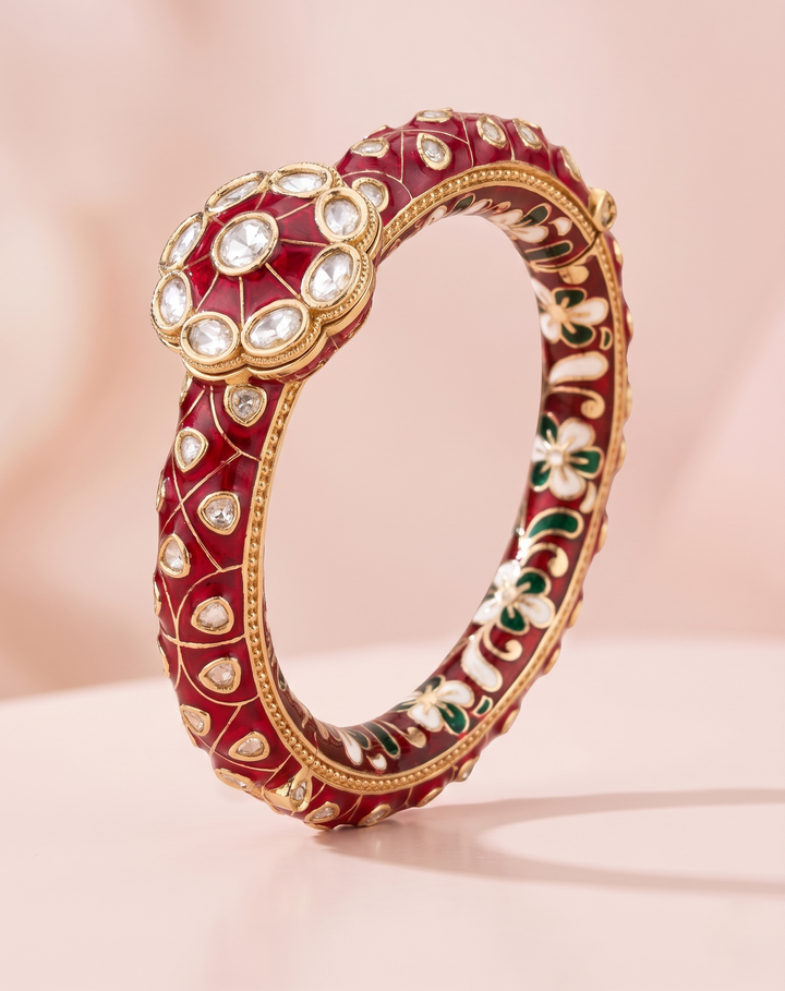 Decorative red bangle with gold and gemstone accents on a light pink background