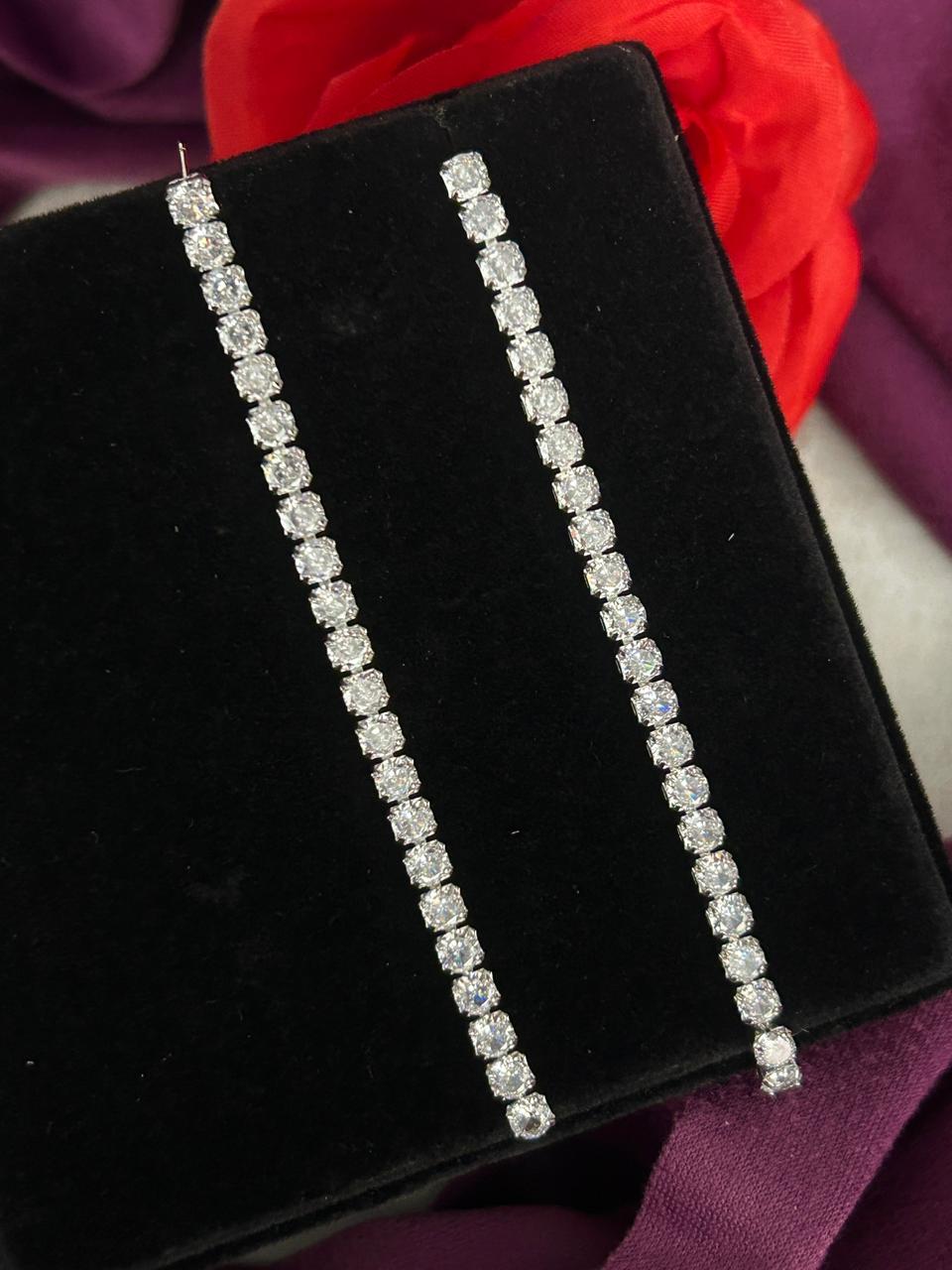 Diamond earrings on a black velvet stand with a red flower in the background