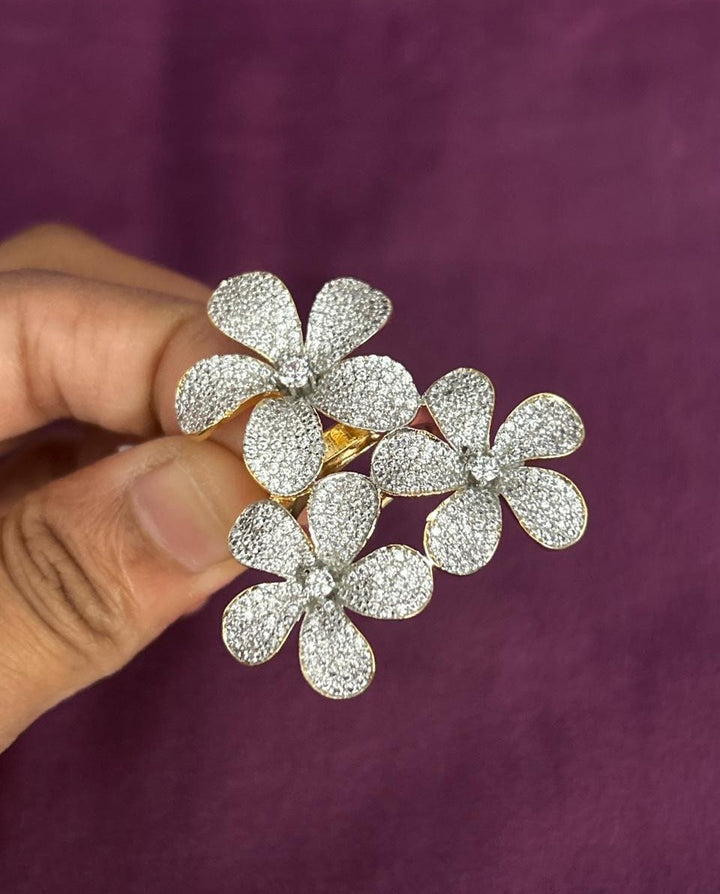 Diamond flower ring held by a hand against a purple background