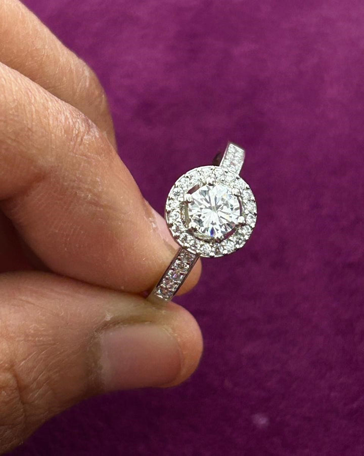 Diamond ring held between fingers against a purple background