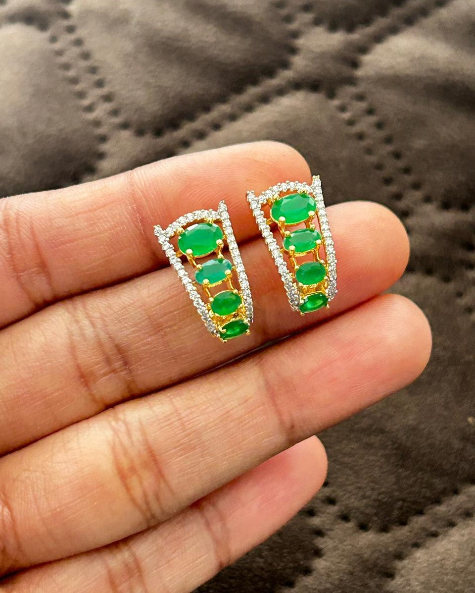 Earrings with green gemstones held between fingers against a textured gray background