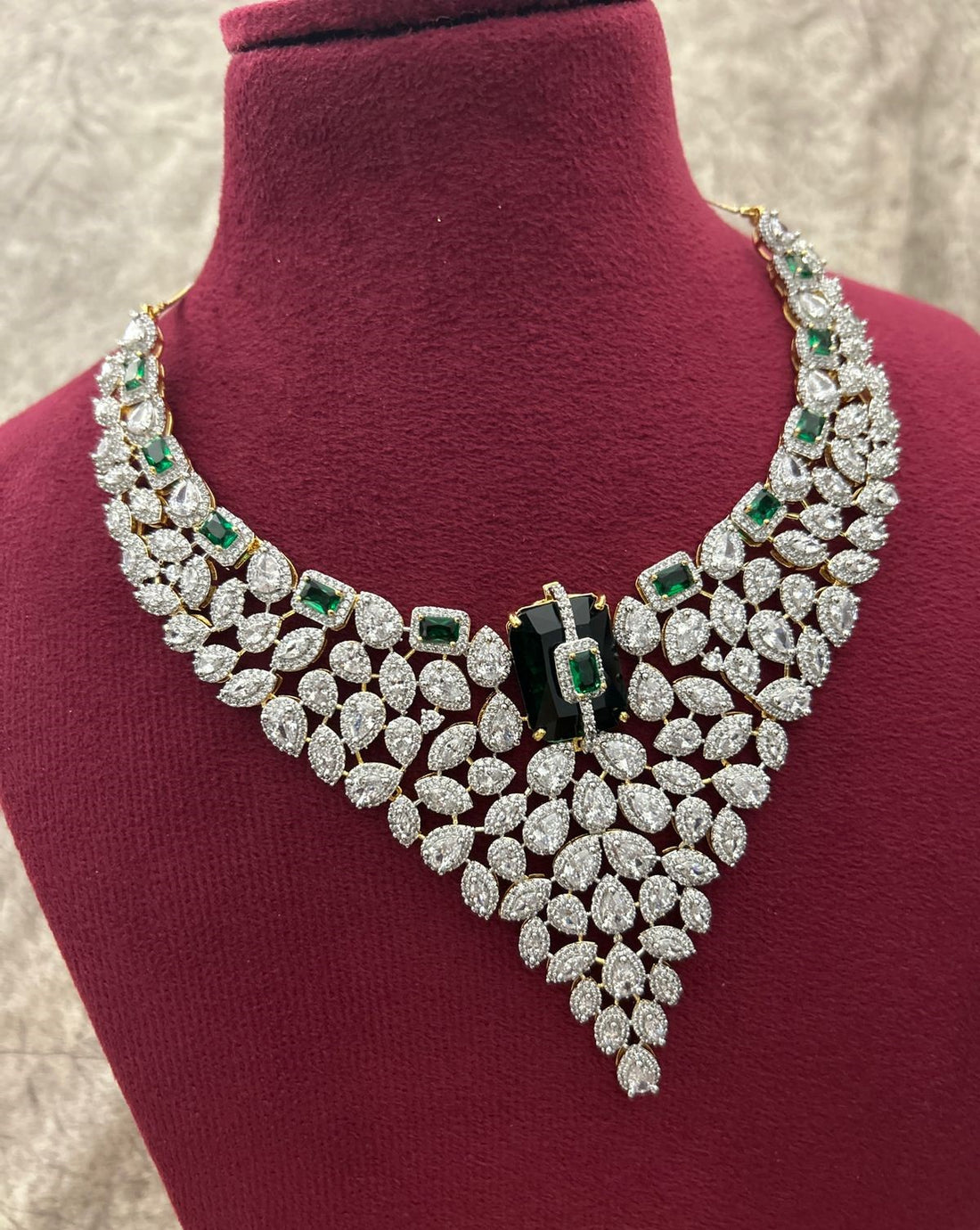 Elegant diamond necklace with green gemstones on a mannequin bust.