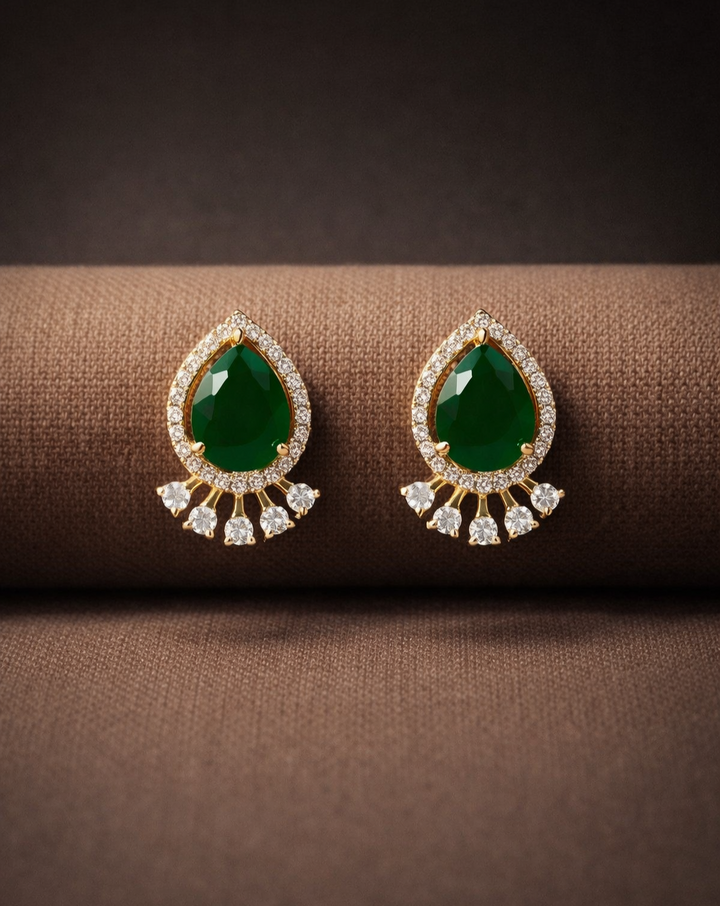 Pair of green gemstone earrings with gold and diamond accents on a brown fabric background