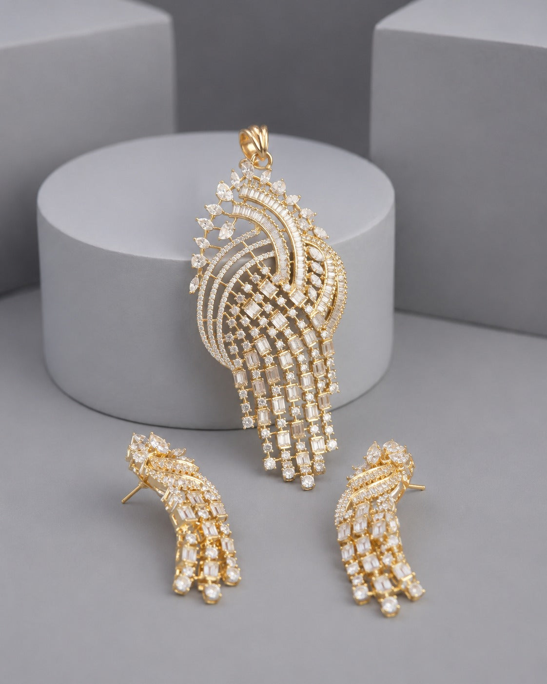 Gold-tone jewelry set featuring a large peacock-shaped pendant and two matching stud earrings, both adorned with clear rhinestones, displayed on a gray background with a cylindrical pedestal.