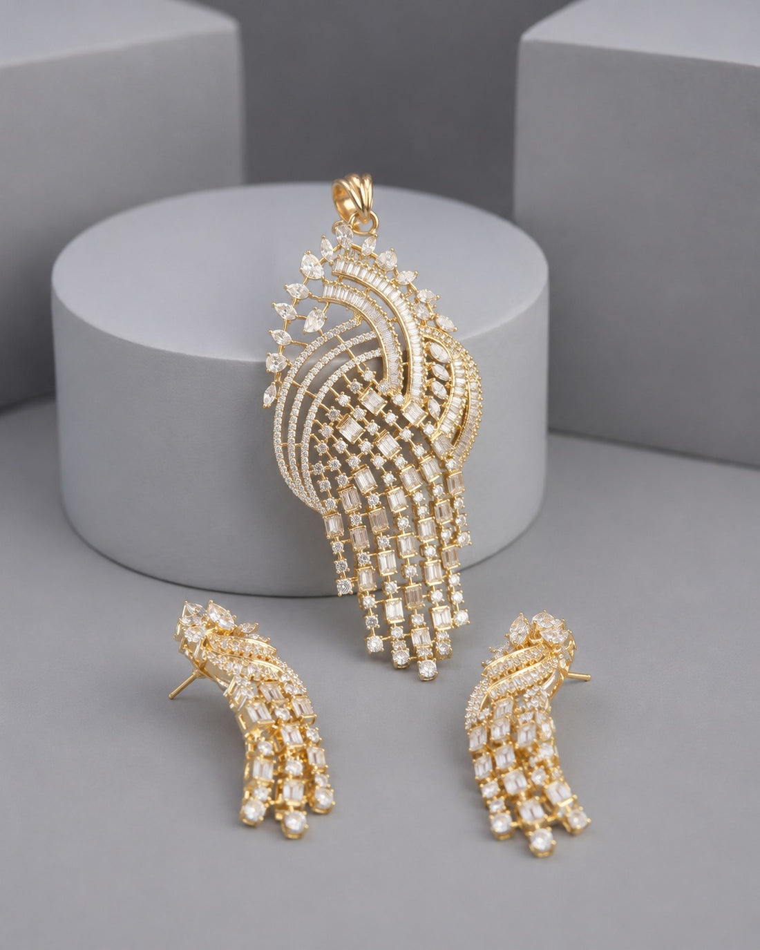 Gold-tone jewelry set featuring a large peacock-shaped pendant and two matching stud earrings, both adorned with clear rhinestones, displayed on a gray background with a cylindrical pedestal.