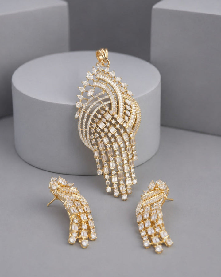 Gold-tone jewelry set featuring a large peacock-shaped pendant and two matching stud earrings, both adorned with clear rhinestones, displayed on a gray background with a cylindrical pedestal.