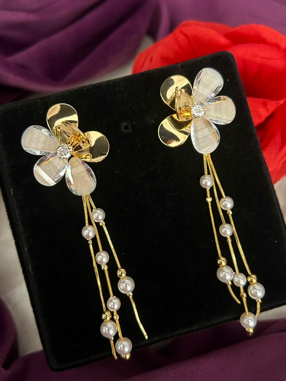 Floral earrings with gold and pearl details on a black stand against a purple fabric background
