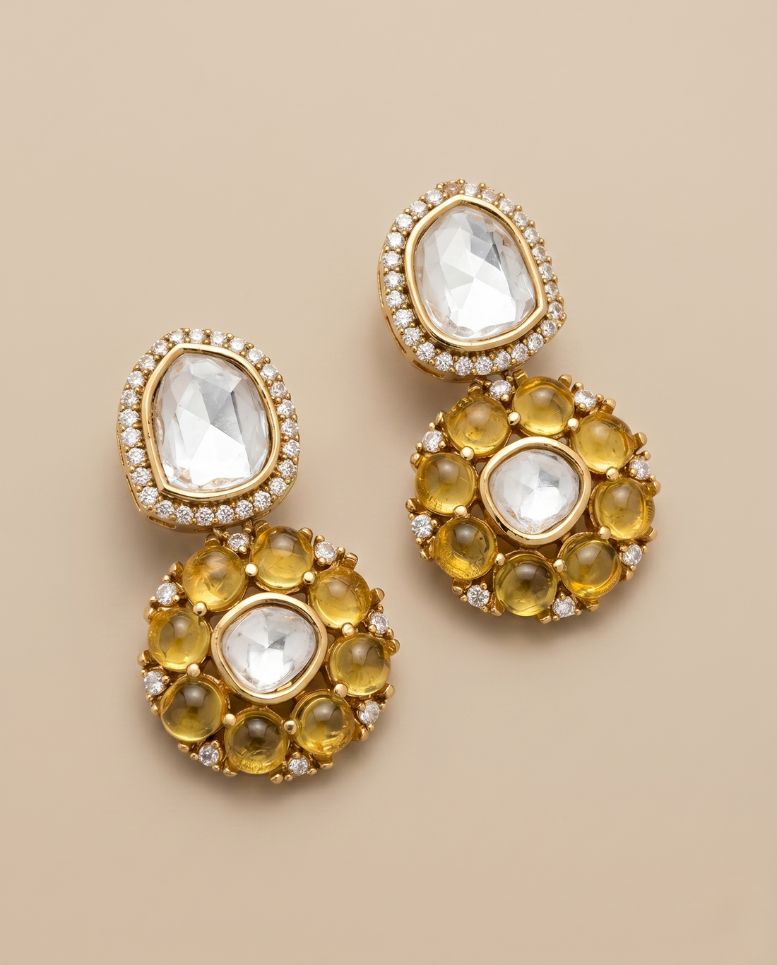 Gold earrings with clear and yellow gemstones on a beige background