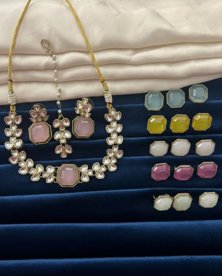 Jewelry set including necklace and earrings on a blue surface with a beige fabric background.