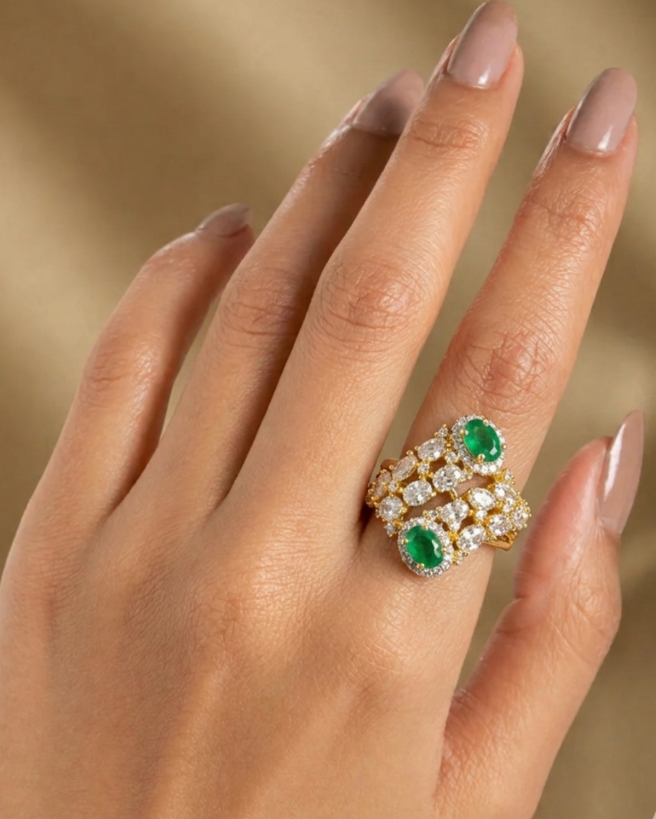 Gold ring with emeralds on a hand against a beige background