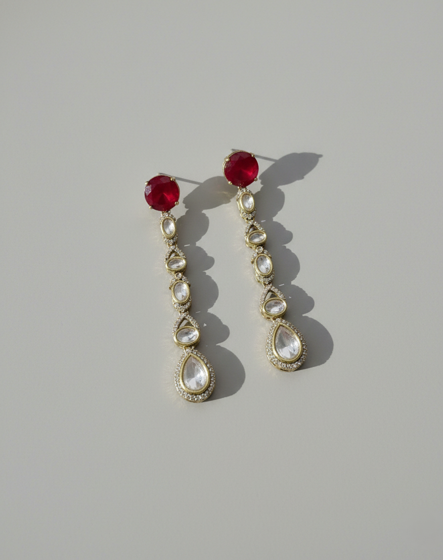 Pair of earrings with red gemstones and teardrop-shaped pearls on a gray background
