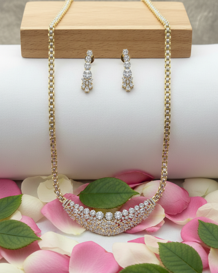 Necklace and earrings set on a white surface with pink petals and green leaves.