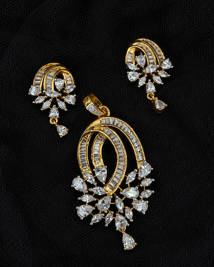 Gold-tone jewelry set featuring a large pendant and matching earrings, both adorned with clear gemstones, displayed on a textured black fabric background.