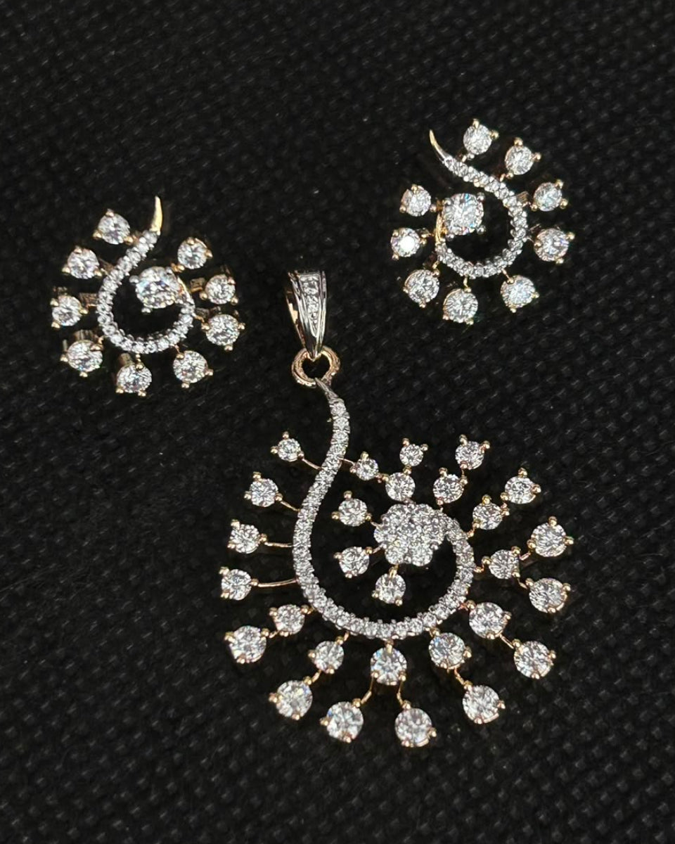 A gold-plated jewelry set featuring a large paisley-shaped pendant and matching stud earrings, both heavily embellished with clear stones, displayed on a textured black background.