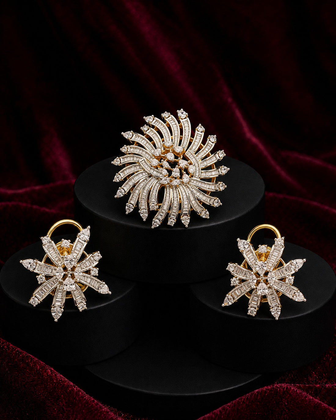 A gold-tone jewelry set featuring a large sunburst brooch and two matching snowflake-shaped earrings, both adorned with clear pavé stones, displayed on black pedestals against a dark red velvet background.