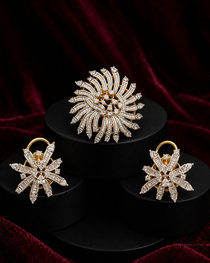 A gold-tone jewelry set featuring a large sunburst brooch and two matching snowflake-shaped earrings, both adorned with clear pavé stones, displayed on black pedestals against a dark red velvet background.