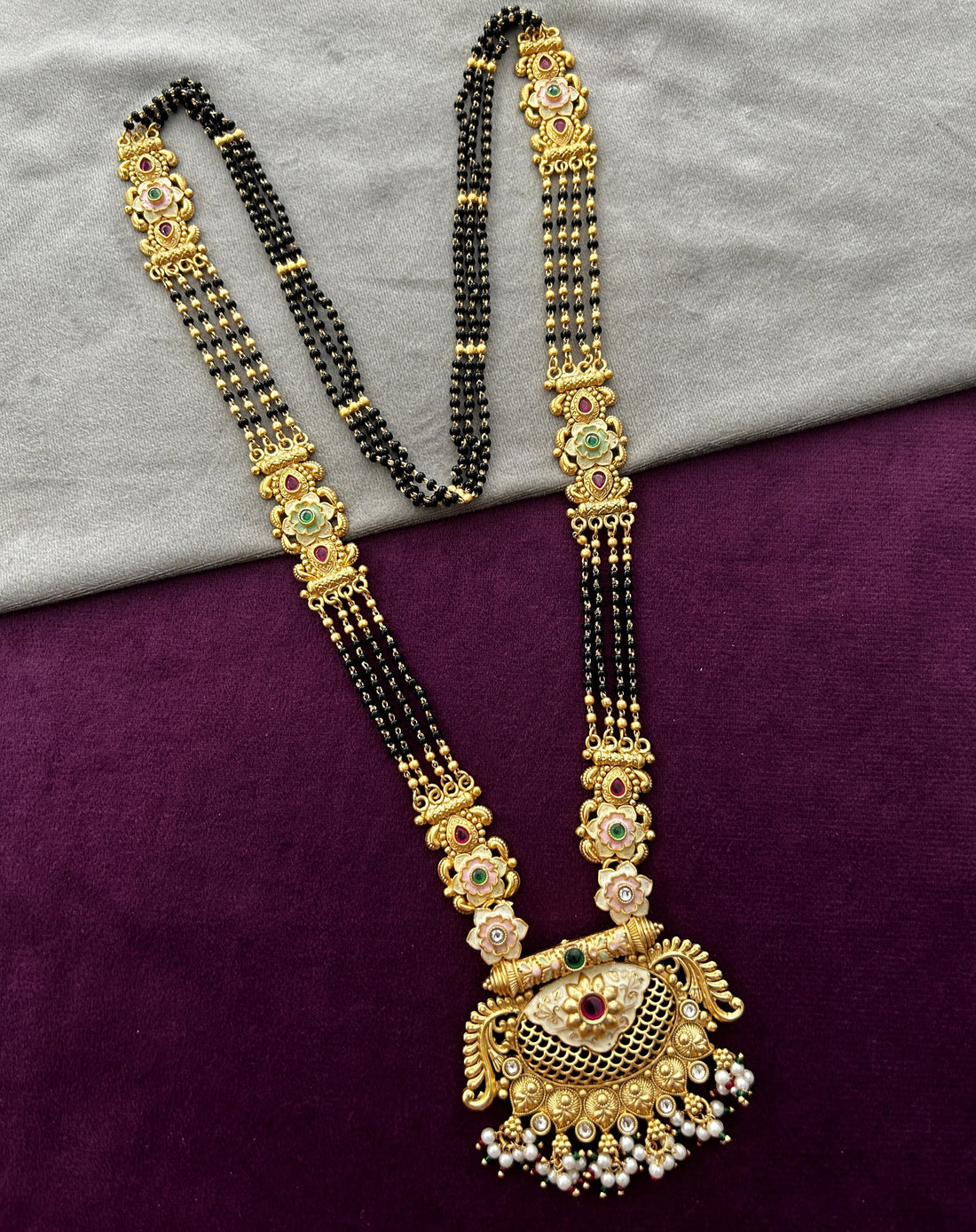 Gold and black beaded necklace on a gray and purple fabric background