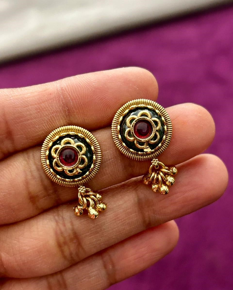 Gold and black earrings with red gemstones held in a hand against a purple background