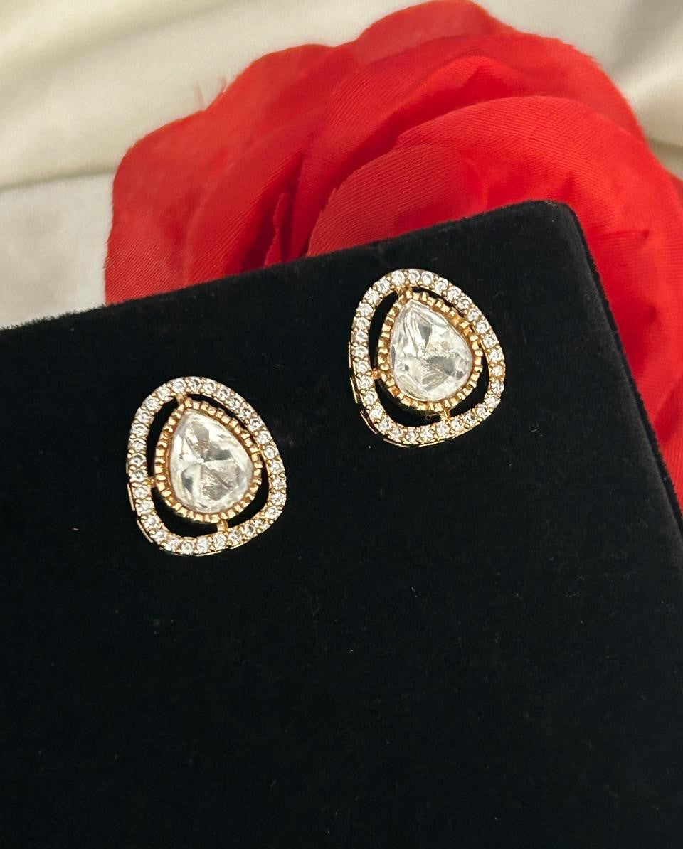 Gold and clear teardrop earrings on a black stand with red fabric in the background