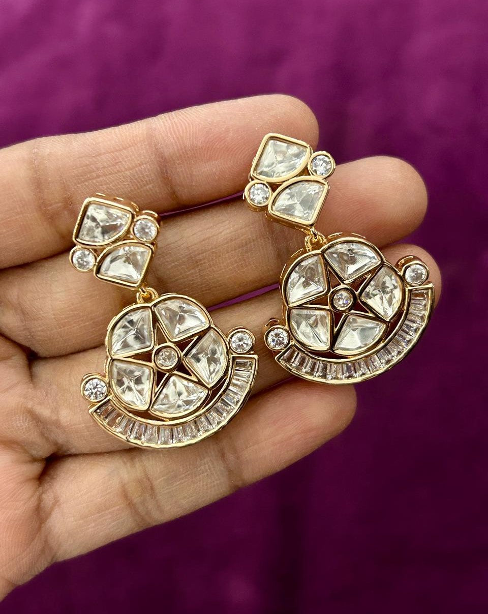 Gold and crystal earrings held in a hand against a purple background