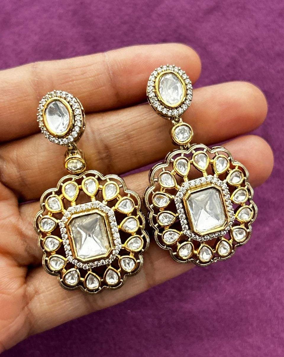 Gold and crystal earrings held between fingers against a purple background