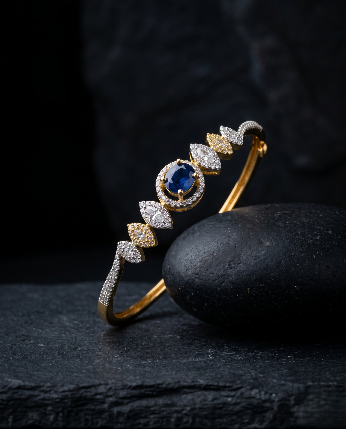 Gold and diamond bracelet with a blue gemstone on a dark stone surface