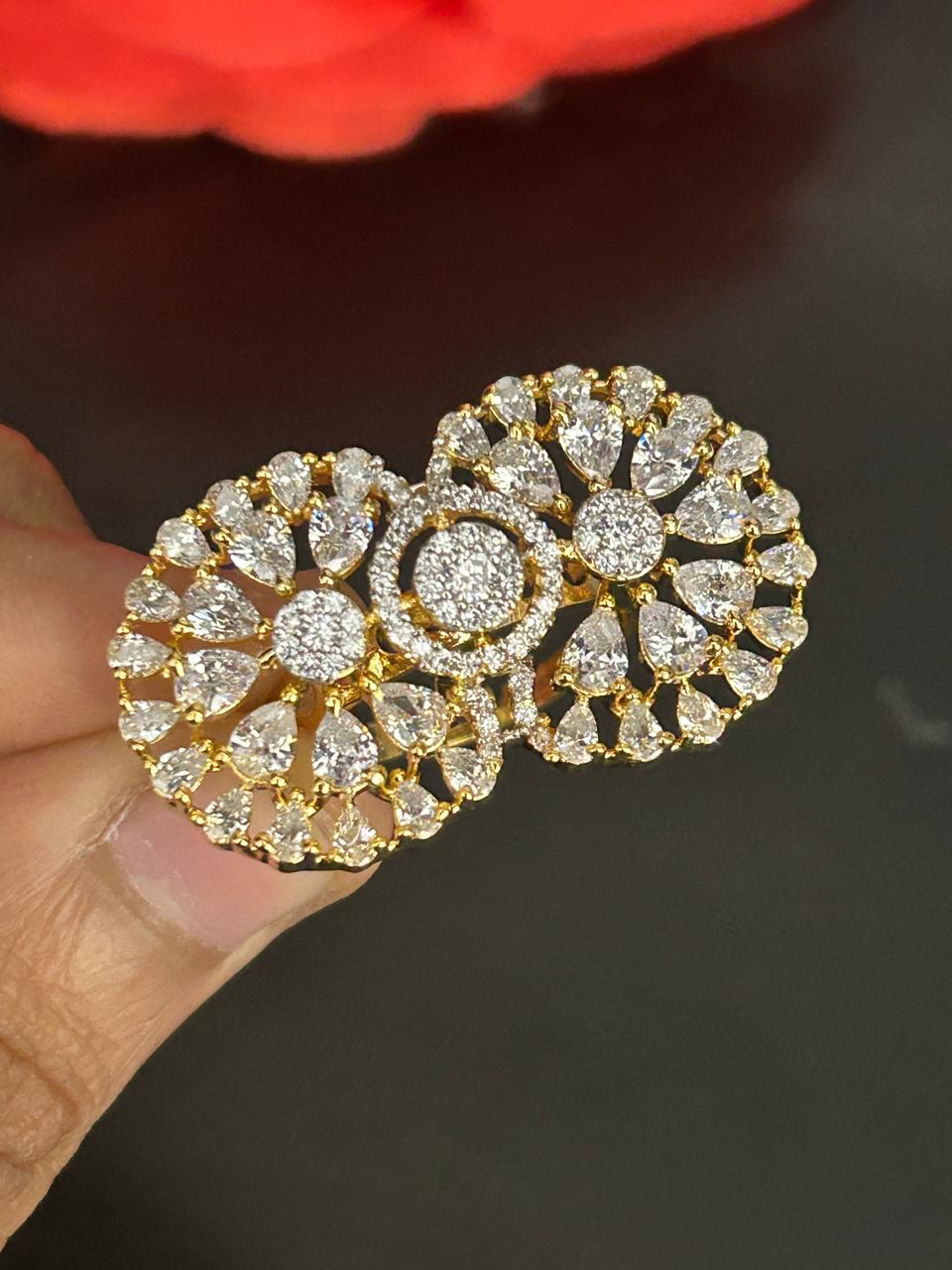 Gold and diamond earrings held by a hand against a dark background