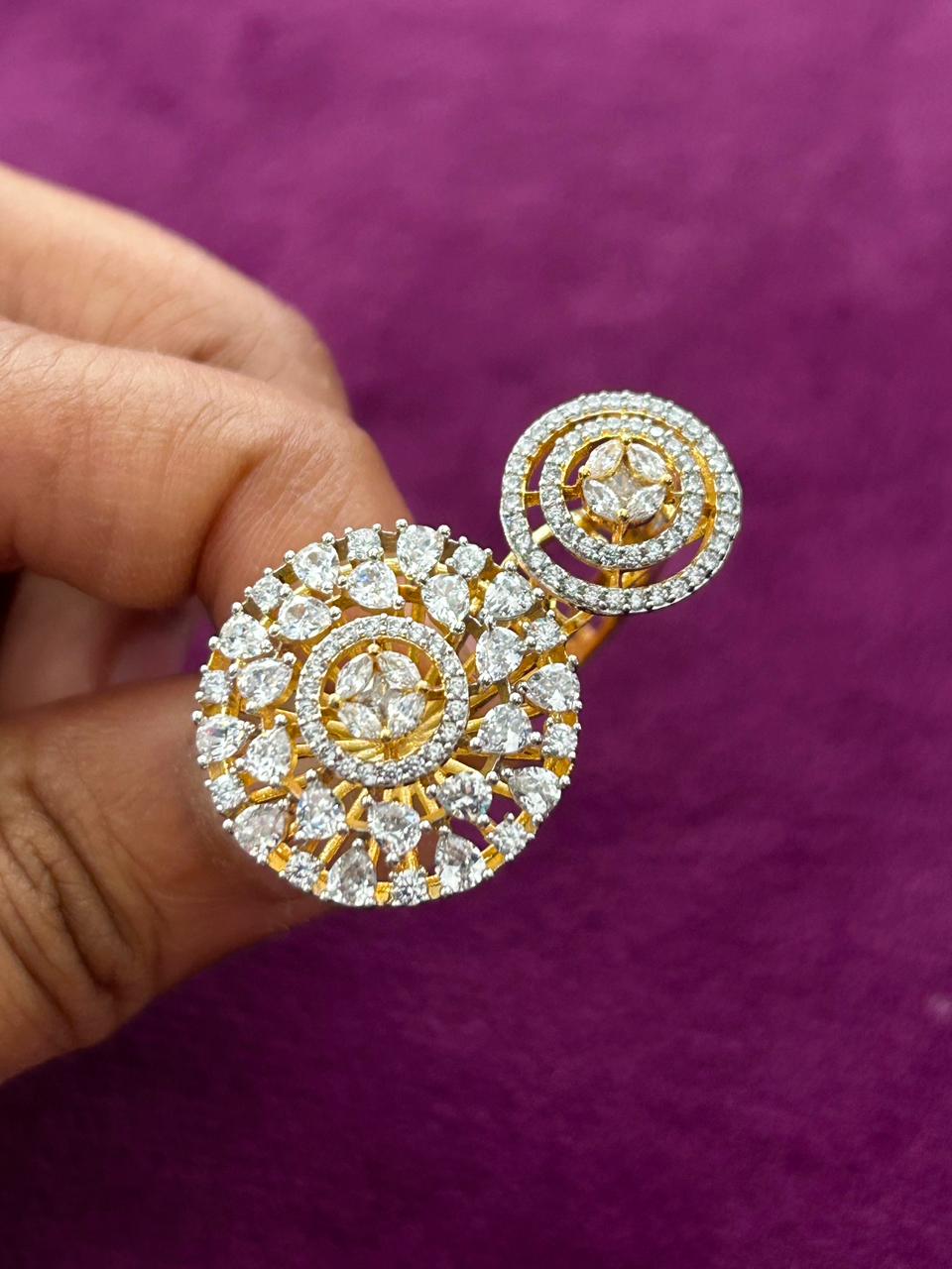 Gold and diamond earrings held by a hand against a purple background