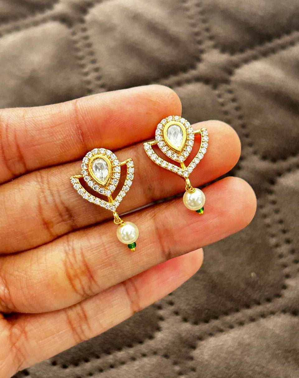 Gold and diamond earrings with pearls held between fingers on a textured gray background