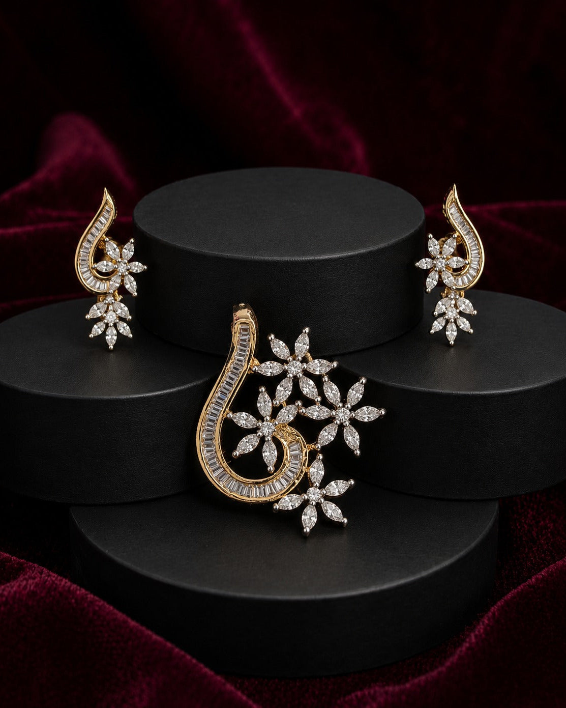 Gold and diamond jewelry set featuring a central paisley- and two matching earrings, displayed on black cylindrical pedestals against a dark red velvet background.