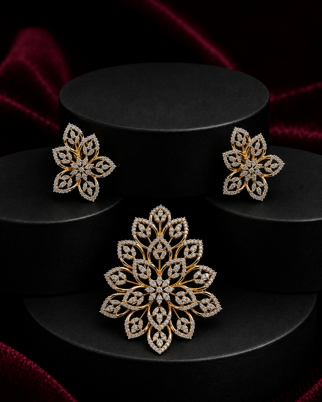 Gold and diamond jewelry set featuring a large floral brooch and matching stud earrings, displayed on black cylindrical pedestals against a dark red velvet background.