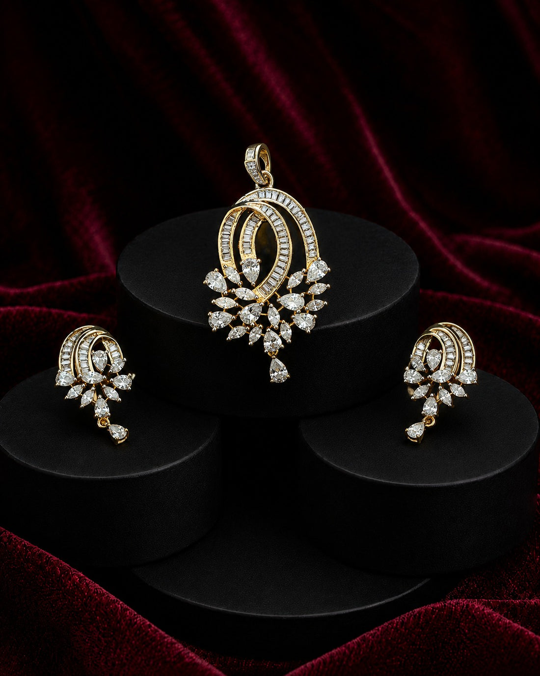 Gold and diamond jewelry set featuring a pendant, earrings, and matching rings displayed on black cylindrical pedestals against a dark red velvet background.