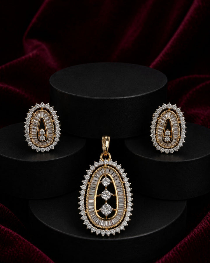 Gold and diamond jewelry set featuring a teardrop pendant and matching earrings, displayed on black cylindrical pedestals against a dark red velvet background.