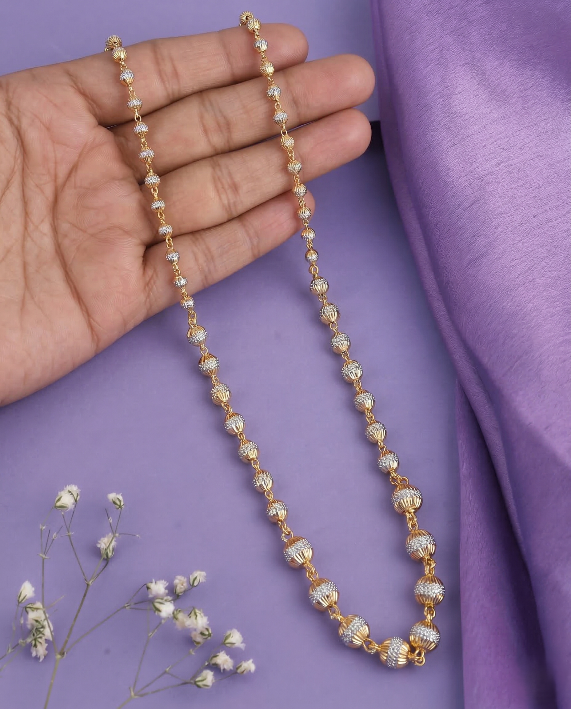 Gold and diamond necklace held by a hand on a purple fabric background